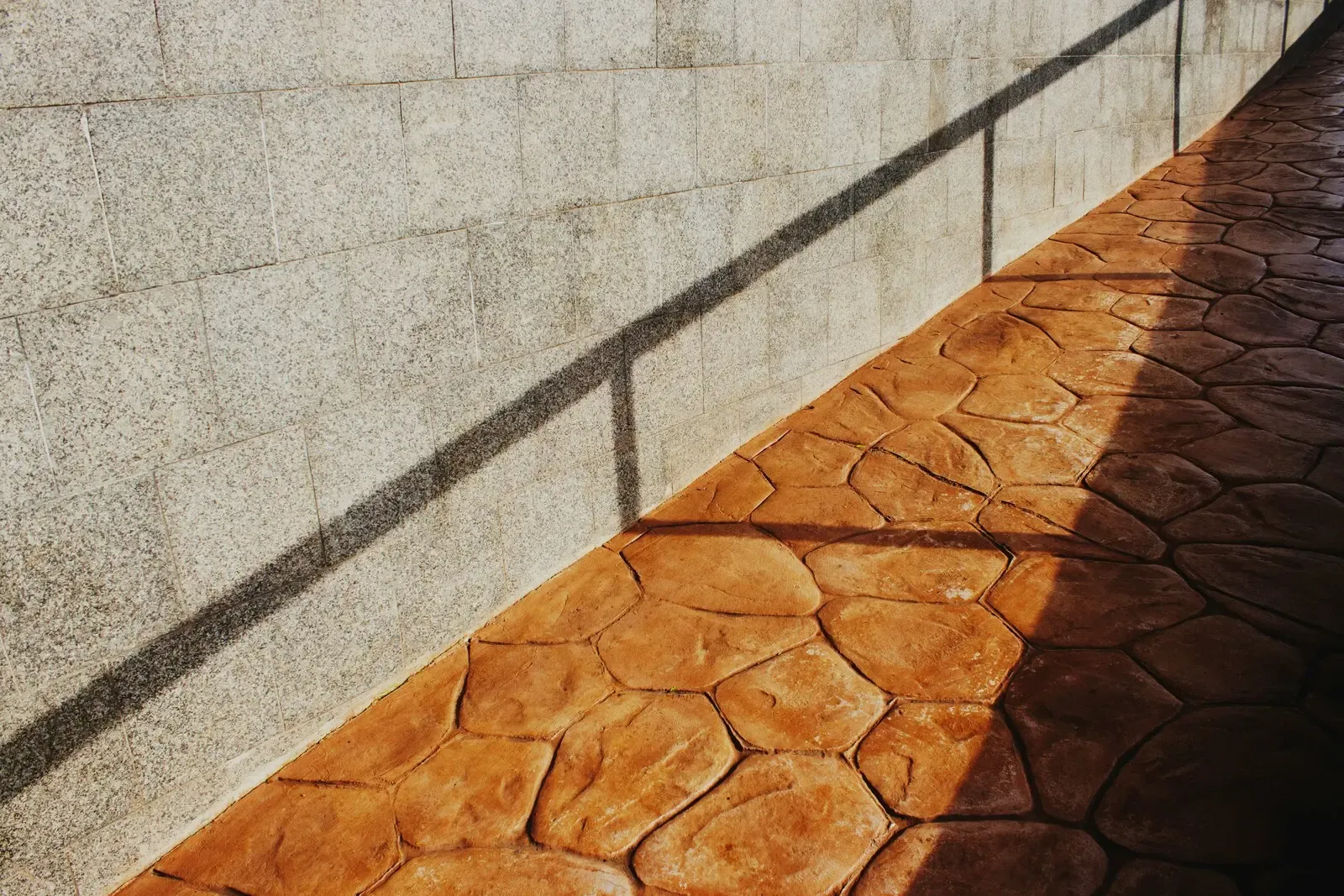A stamped concrete walkway with a hand-tooled stone pattern and integral color, cast beside a wall